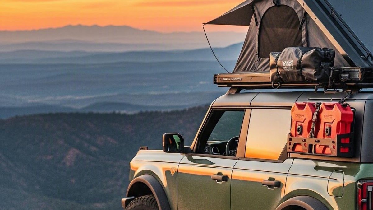 A green off-road vehicle at sunset with a rooftop tent deployed, gear on the roof rack, and red fuel containers mounted on the side, set against a mountainous landscape.
